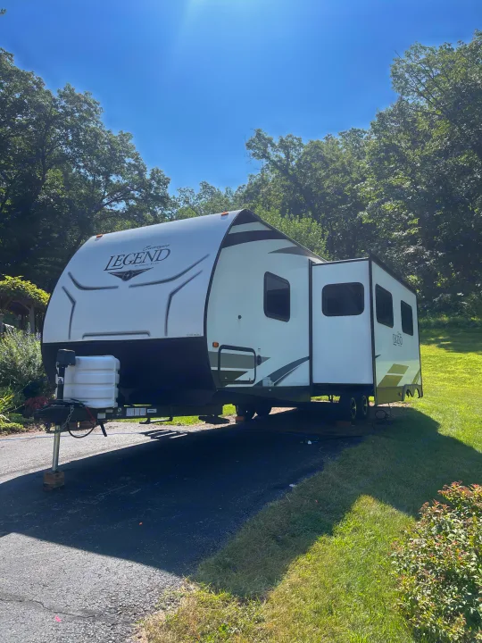 White Legend travel trailer, slide-out extended, parked on a driveway. Great for an RV rental adventure.. Forest River Surveyor Legend 2019