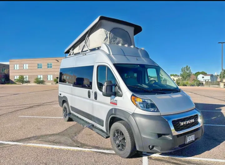 This silver Ram ProMaster camper van, with its pop-top tent extended, is parked and ready. Ideal for an RV rental and camping adventures.. Thor Motor Coach 18T 2022