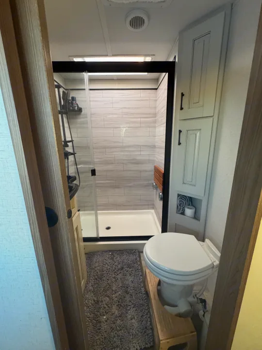 Inside a clean, organized RV rental bathroom featuring a sleek shower, toilet, and storage.. Alliance Paradigm 2023