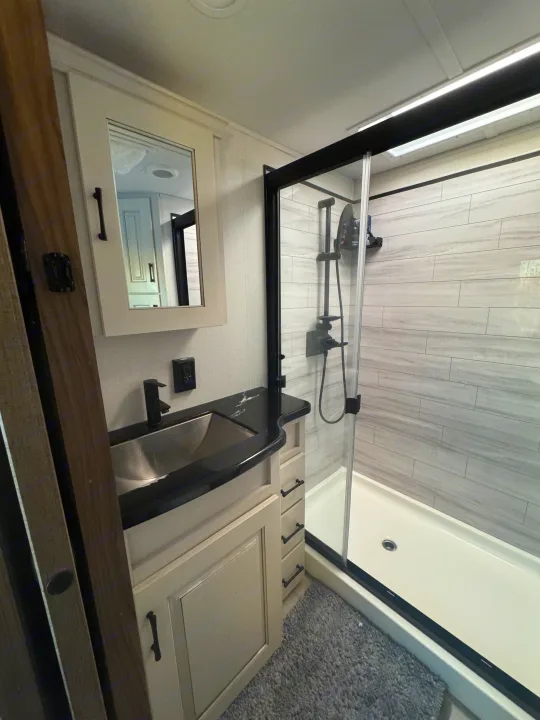 RV rental bathroom: modern vanity with black sink & counter, medicine cabinet, and glass-enclosed shower with gray tiled walls.. Alliance Paradigm 2023