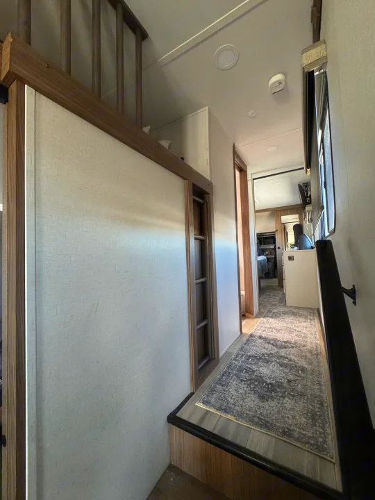 RV rental interior showcasing a modern hallway with light walls, wood trim, step-down, and a cozy rug.. Alliance Paradigm 2023