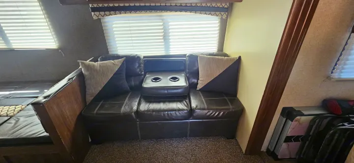 Relax in this RV rental's cozy interior, featuring a dark leather sofa with cup holders, pillows, and window blinds.. Heartland RVs Prowler Lynx 2018