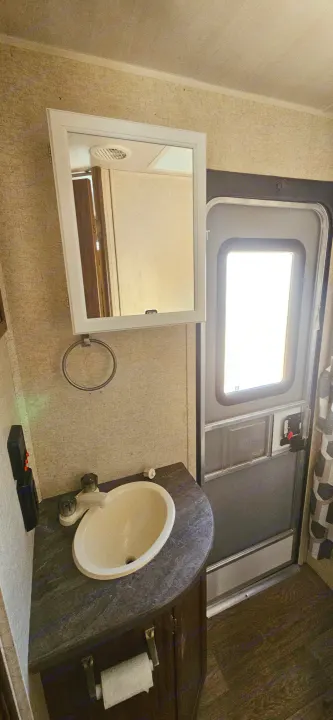RV rental bathroom showing a compact sink, vanity, mirror, and a bright external access door.. Heartland RVs Prowler Lynx 2018