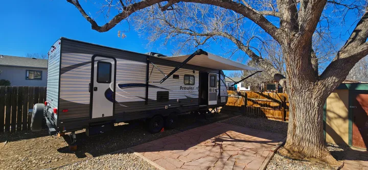 This Prowler Lynx travel trailer RV rental is parked on a gravel lot with its awning extended beside a patio.. Heartland RVs Prowler Lynx 2018