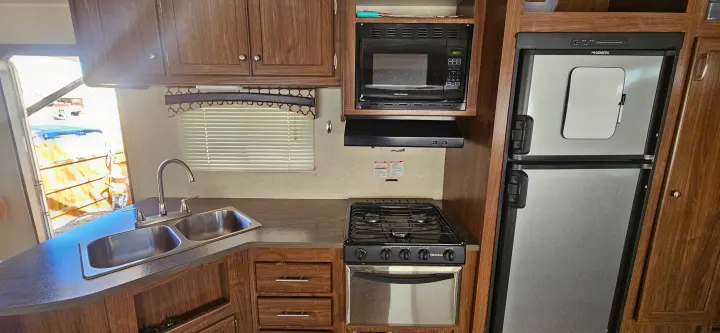 RV rental interior: This compact kitchen offers a double sink, stove, microwave, and Dometic fridge, perfect for your travels.. Heartland RVs Prowler Lynx 2018
