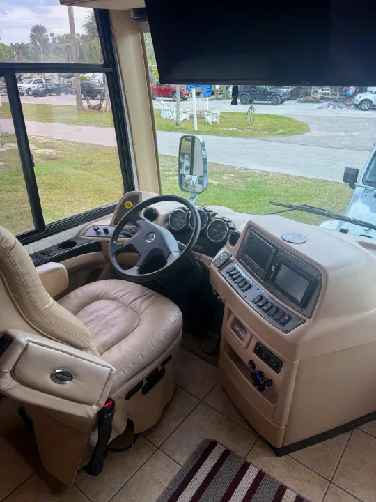 Spacious RV rental driver's area with comfortable beige seat, detailed dashboard, and a view of the campground outside.. Kountry Star Kountry Star Motorhome 2008