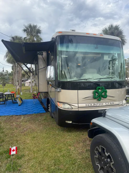 A large Kountry Star RV rental is set up with an awning, blue patio mats, outdoor furniture, and a green shamrock wreath.. Kountry Star Kountry Star Motorhome 2008