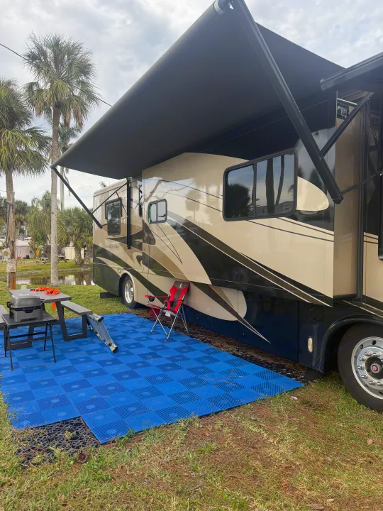 Spacious rv rental motorhome with extended awning, picnic table, grill on a blue mat, surrounded by palm trees and nature.. Kountry Star Kountry Star Motorhome 2008