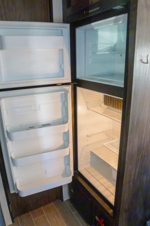 Empty two-door RV rental fridge and freezer with open doors, ready for your adventure supplies.. Forest River Cherokee Wolf Pup Black Label 2020