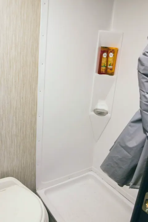 Compact RV rental bathroom with shower, built-in shelf, and toilet, offering essential amenities.. Forest River Cherokee Wolf Pup Black Label 2020