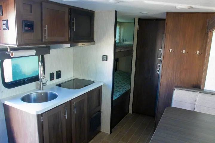 RV rental interior: kitchen with sink & stovetop, bunk beds, dining area. Furrion controls and coat hooks visible.. Forest River Cherokee Wolf Pup Black Label 2020