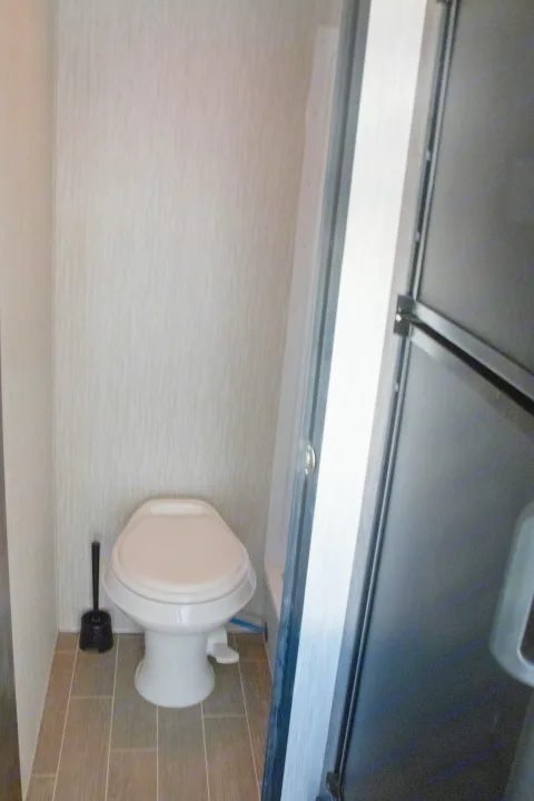 A clean, compact RV rental bathroom showing a white toilet, plunger, and wood-look flooring. Ideal for small spaces.. Forest River Cherokee Wolf Pup Black Label 2020