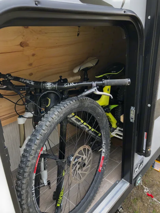 Two mountain bikes are efficiently stored inside an RV rental compartment, featuring wooden walls and tile flooring.. Forest River Cherokee Wolf Pup Black Label 2020