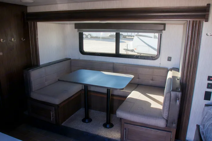 U-shaped RV rental dinette with gray upholstered seating, a table, and natural light from window.. Forest River Cherokee Wolf Pup Black Label 2020