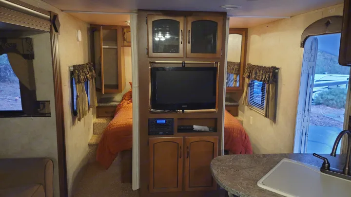 RV rental interior features a cozy bedroom, entertainment area with TV, & kitchenette. Ideal for adventure!. Keystone RV Springdale 2012