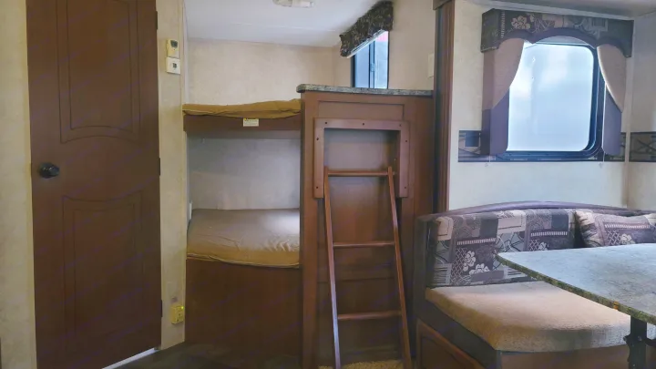 RV rental interior: bunk beds with a ladder, plus a dinette area featuring patterned seating cushions and a window.. Keystone RV Springdale 2012