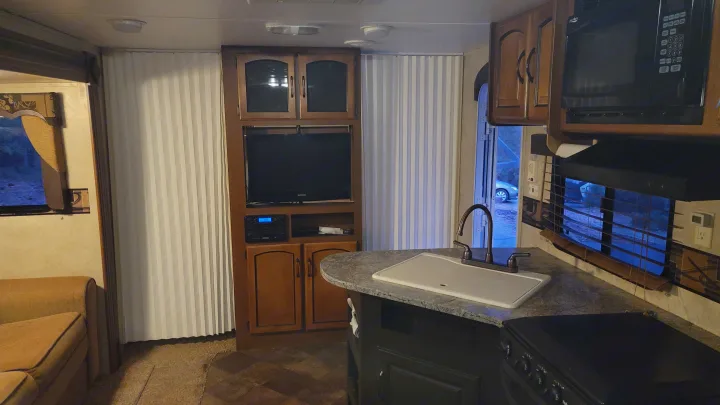 This inviting RV rental interior features a kitchen with sink, entertainment area with TV, and comfortable sofa.. Keystone RV Springdale 2012