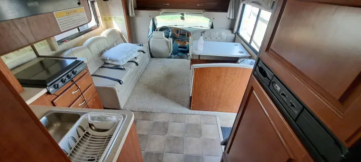 Inside an RV rental: a compact kitchen, sofa bed, dining booth, and driver's cockpit. Ready for your next adventure.. Four Winds Chateau 2007
