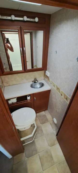 A functional RV rental bathroom featuring a sink, toilet, overhead lights, and a mirrored vanity.. Four Winds Chateau 2007