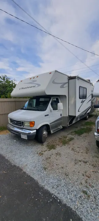 White Ford Chateau Class C motorhome, an ideal RV rental, parked on gravel. Includes slide-out for spacious living. KHT-78X.. Four Winds Chateau 2007