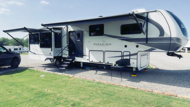 This Paradigm fifth-wheel RV rental is perfectly set up at a sunny campsite, with awnings extended & steps down.. Alliance Paradigm 2023