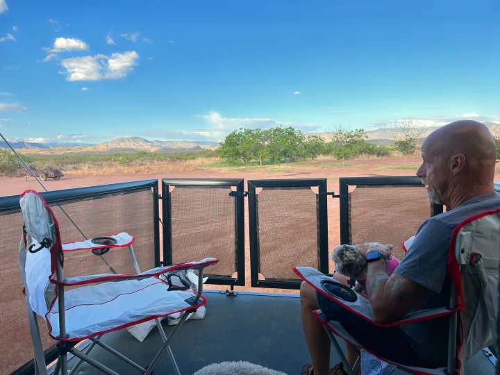 RV rental: Man and dog relax on deck chairs, enjoying a scenic desert view from their RV. Ideal for pet-friendly outdoor escapes.. Grand Design Momentum Toy Hauler 2022