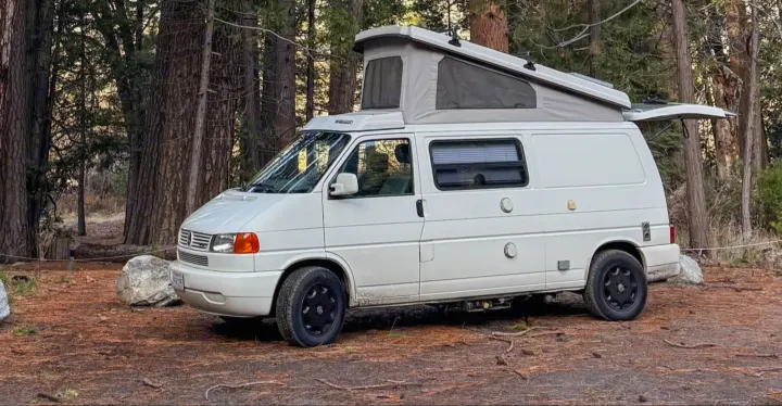 This white pop-top camper van RV rental is set up for camping in a beautiful forest clearing.. Winnebago Eurovan Camper Eurovan Camper 1999