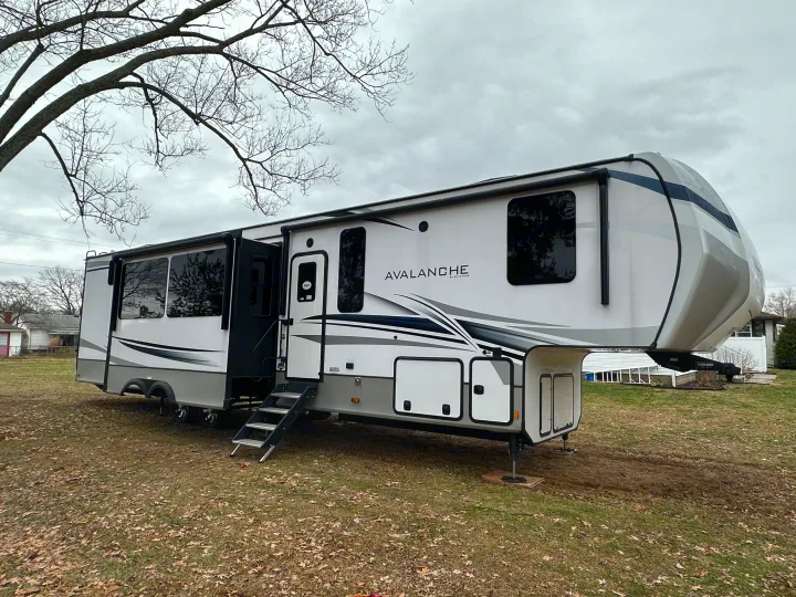 This large white and grey Avalanche fifth-wheel RV is parked on a grassy yard, slides extended, perfect for an rv rental.. Keystone RV Avalanche 2023