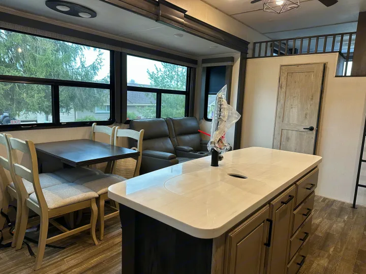 RV rental interior showcasing a modern kitchen island, dining area with chairs, and reclining sofa, designed for comfort.. Keystone RV Avalanche 2023