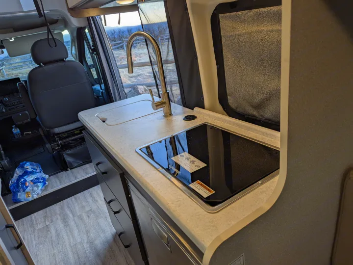 This RV rental interior showcases a functional kitchen counter with sink, faucet, and a Dometic cooktop, ready for your road trip.. Thor Dazzle 2024
