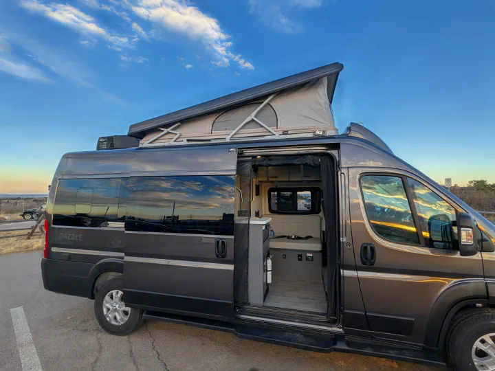 Gray pop-top camper van, perfect for your next RV rental adventure. Interior visible through open side door.. Thor Dazzle 2024