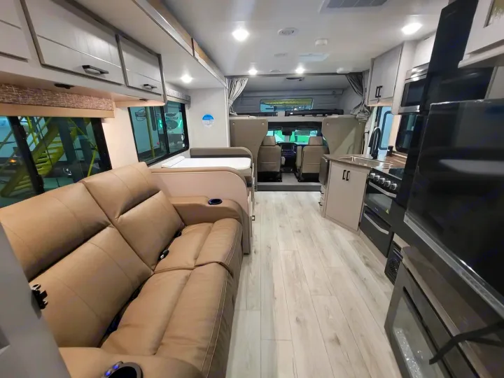 Inside a bright RV rental: modern interior with a comfy reclining sofa, dinette, full kitchen, and light wood floors.. Couchmen Entourage 340BH 2025