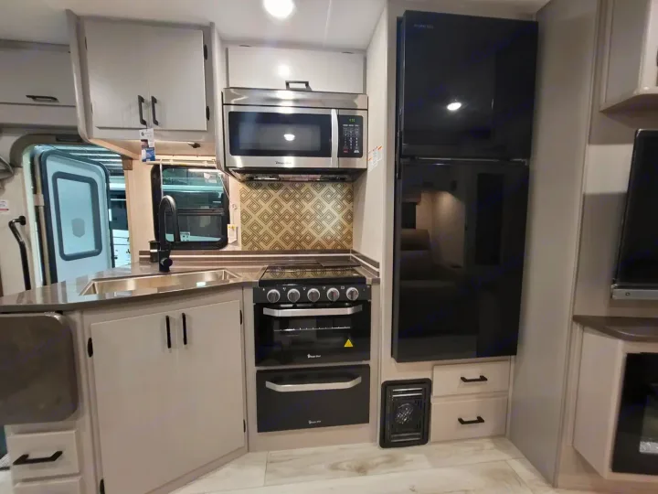 Explore this modern RV rental kitchen. Features include a sink, black appliances (microwave, stove, oven, fridge), and light cabinets.. Couchmen Entourage 340BH 2025
