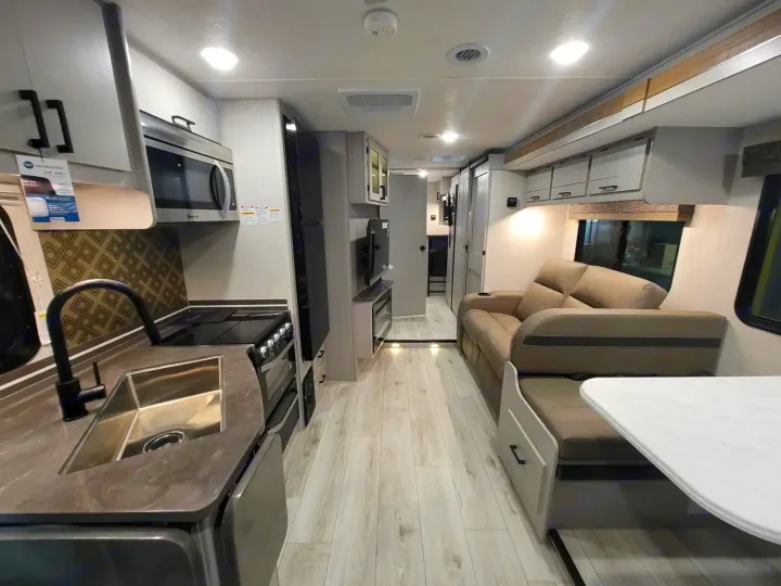 Inside a modern RV rental: well-equipped kitchen with stove, microwave, sink; comfortable living space with sofa and dining.. Couchmen Entourage 340BH 2025