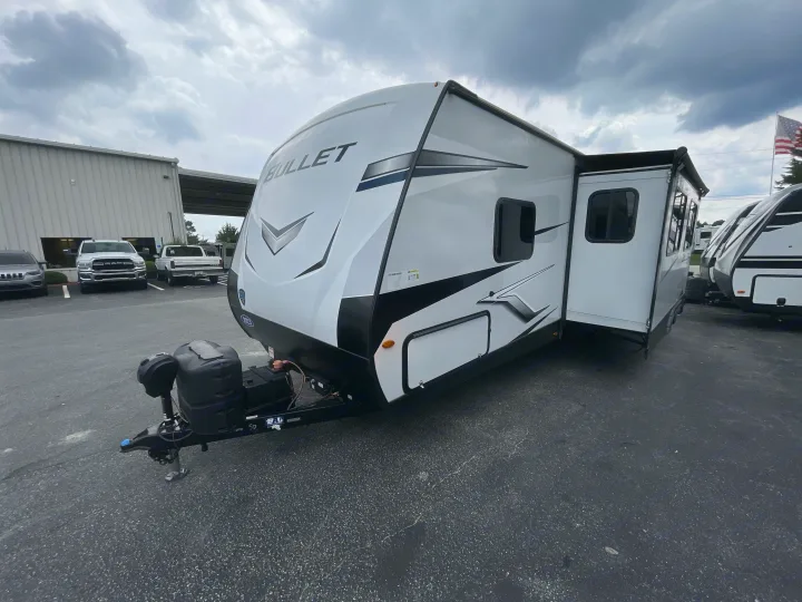 White "Bullet" travel trailer, a spacious RV rental, parked on asphalt with a slide-out extended.. Keystone Bullet 2023