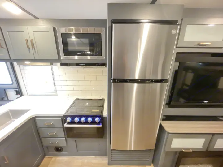 Sleek RV rental kitchen: stainless steel fridge, microwave, range, sink, grey cabinets, white counters, and TV.. Keystone Bullet 2023