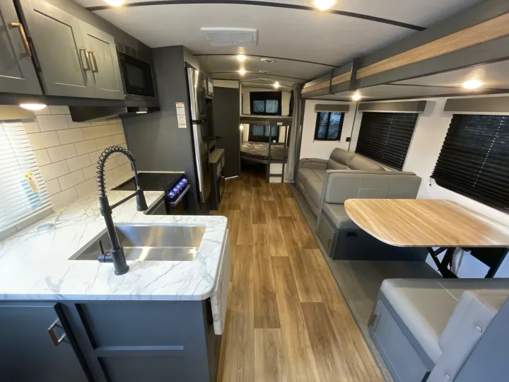 Explore this modern RV rental interior, featuring a full kitchen with microwave & sink, dinette, sofa, and bunk beds.. Keystone Bullet 2023