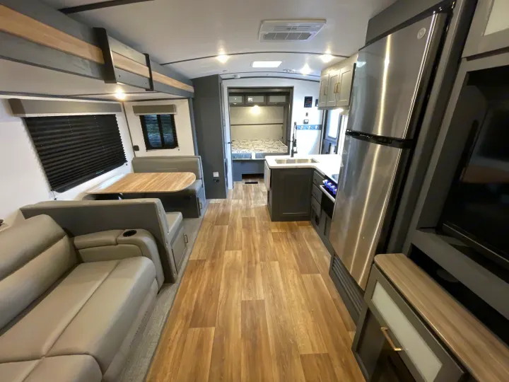Spacious RV rental interior with modern living area, dinette, kitchen, and rear bedroom. Features wood-look flooring and neutral decor.. Keystone Bullet 2023