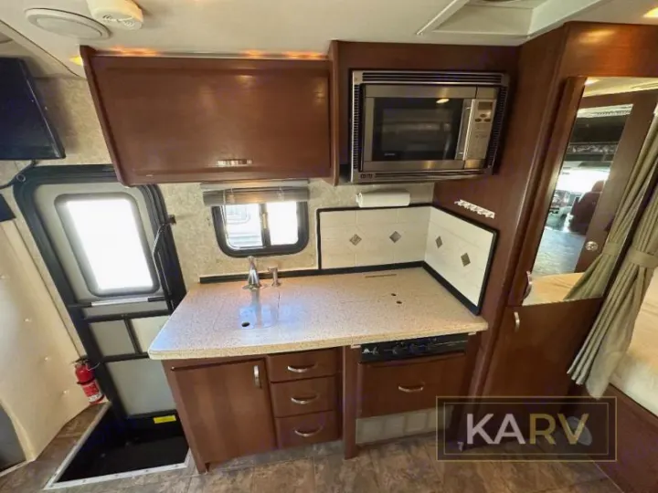 RV rental interior with a compact kitchenette: sink, microwave, stove, cabinets, and an entryway visible.. Fleetwood Tioga 2011