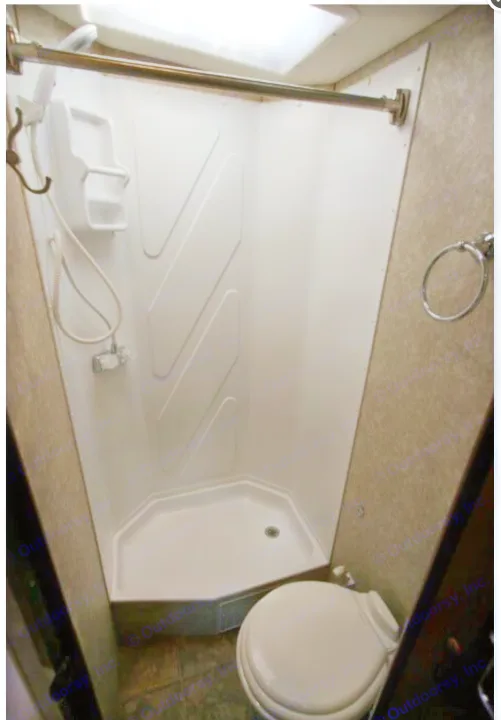 RV rental bathroom with a white compact corner shower, handheld shower head, toilet, and wall-mounted towel ring.. Fleetwood Tioga 2011