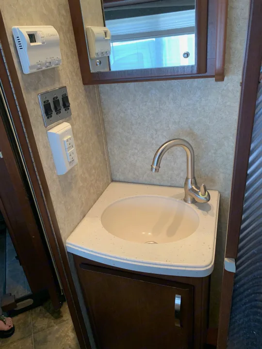 RV rental interior: compact bathroom vanity with sink, faucet, Dometic thermostat, light switches for RV systems, and an outlet.. Fleetwood Tioga 2011