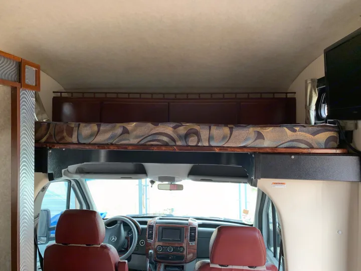 RV rental interior: Front cab features a bed above, dashboard, and red leather seats, ideal for travel.. Fleetwood Tioga 2011