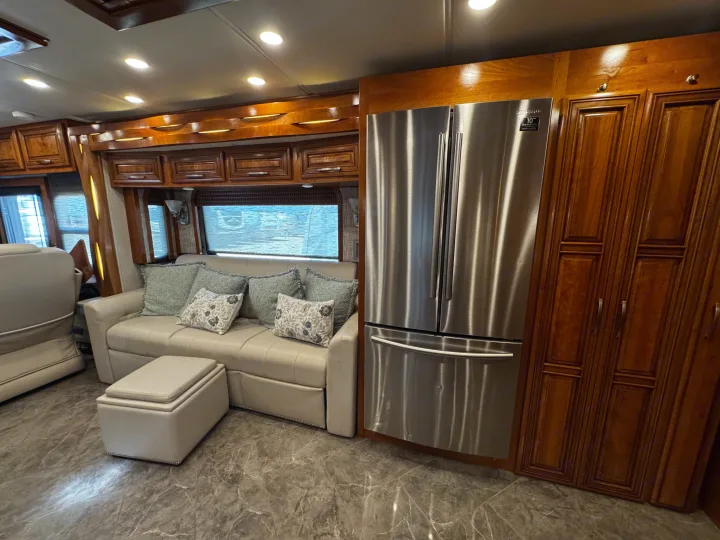 Spacious RV rental interior featuring a modern Samsung fridge, plush sofa, storage ottoman, and rich wood cabinetry.. New Aire New Aire Motorhome 2020