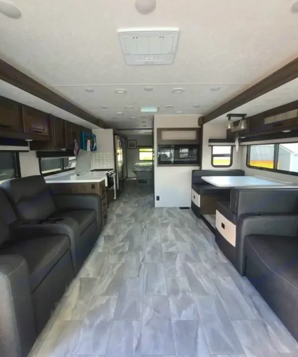 Modern RV rental interior: living space with recliners, kitchen, and dinette. Grey floor and wood accents.. Coachmen Mirada 2024