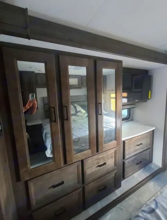 RV rental bedroom: wooden mirrored wardrobe, drawers, and mounted TV for comfortable living and storage.. Coachmen Mirada 2024