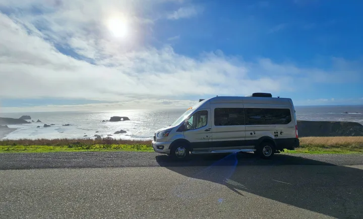 Silver RV rental parked by a scenic Pacific coast highway, offering breathtaking ocean views with sea stacks.. Forest River Coachmen Beyond 2023