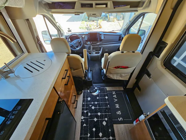 Spacious RV rental interior: modern kitchen with sink, induction cooktop, and full driver's cockpit area.. Forest River Coachmen Beyond 2023
