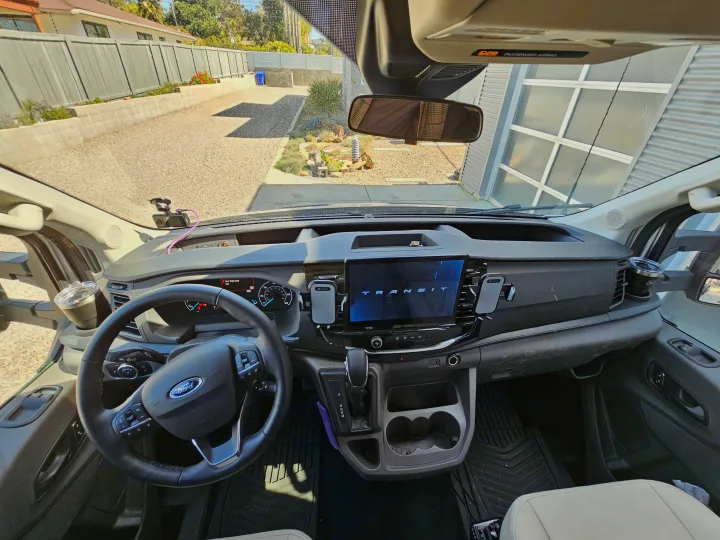 Interior of a spacious Ford Transit van, often used for RV rental, with a clear view of the modern dashboard & digital display.. Forest River Coachmen Beyond 2023