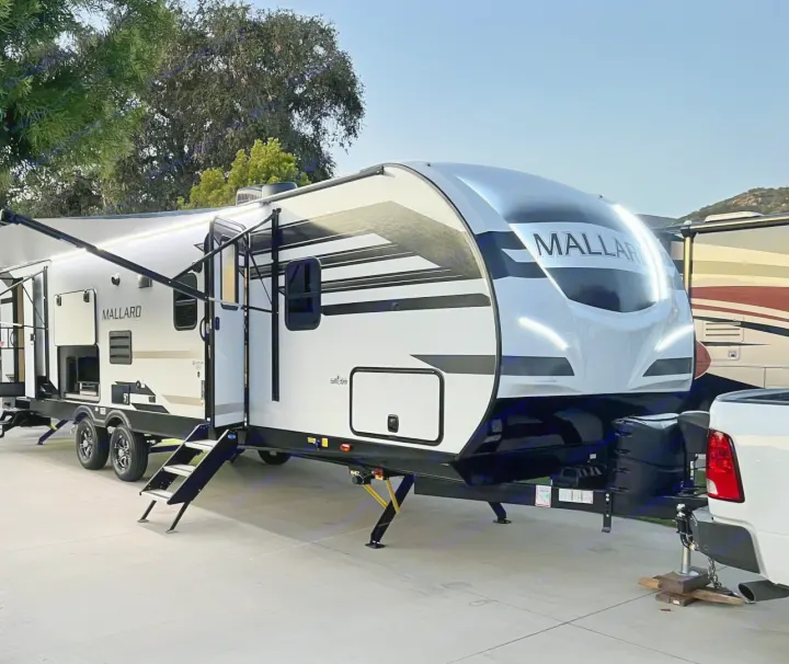 Experience comfort with this modern white and black Mallard travel trailer rv rental, parked with its awning extended and lights on.. Heartland Mallard M312 2022
