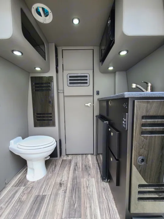 Inside an rv rental: compact kitchen with sink & microwave, fridge, and a toilet. Modern design on wood floor.. Ultimate Toys Ultimate Coach 2026